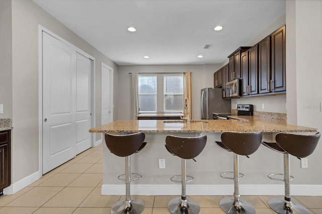 kitchen featuring stainless steel appliances, light stone countertops, kitchen peninsula, a breakfast bar, and sink