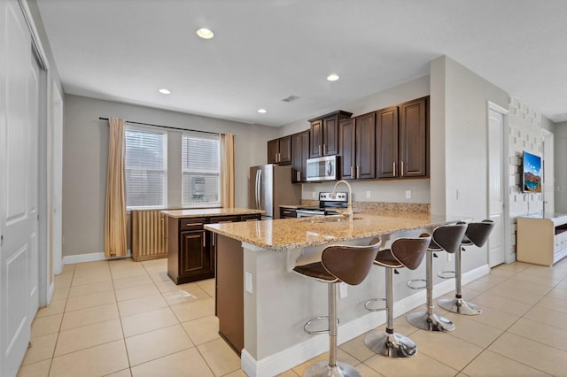 kitchen featuring light stone counters, kitchen peninsula, stainless steel appliances, a breakfast bar, and light tile patterned flooring