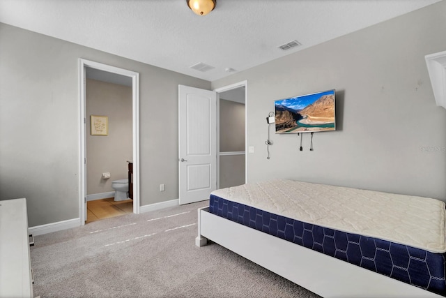 bedroom featuring a textured ceiling, ensuite bathroom, and carpet