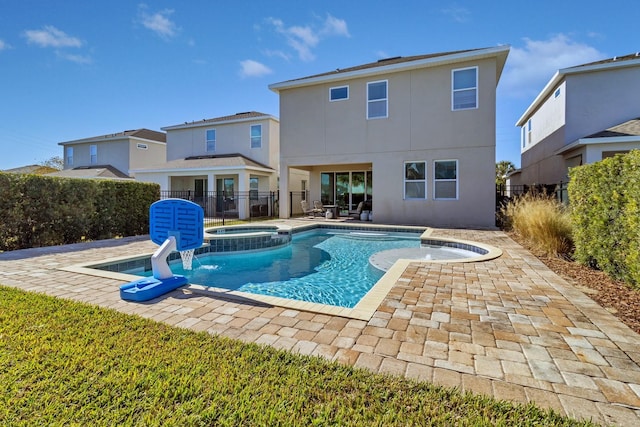 rear view of property featuring a swimming pool with hot tub, a patio, and pool water feature