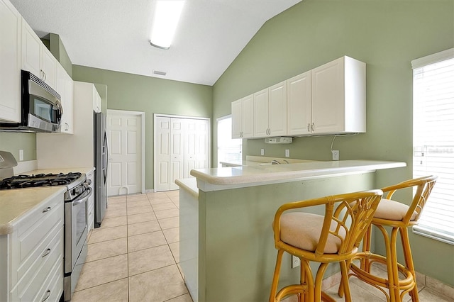 kitchen with white cabinets, appliances with stainless steel finishes, lofted ceiling, a kitchen breakfast bar, and light tile patterned flooring