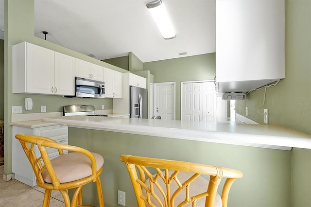 kitchen with white cabinets, appliances with stainless steel finishes, a kitchen breakfast bar, kitchen peninsula, and light tile patterned flooring