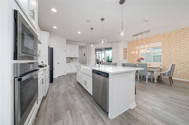 kitchen featuring light hardwood / wood-style flooring, decorative light fixtures, a center island with sink, white cabinets, and appliances with stainless steel finishes