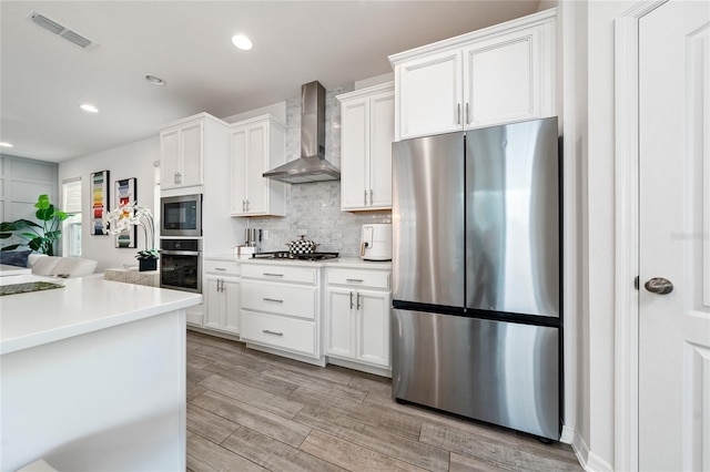 kitchen with decorative backsplash, white cabinetry, stainless steel appliances, and wall chimney range hood