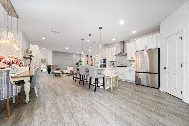 kitchen featuring white cabinets, decorative light fixtures, wall chimney range hood, and stainless steel appliances