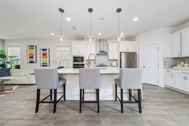 kitchen with a kitchen island with sink, wall chimney exhaust hood, and stainless steel appliances