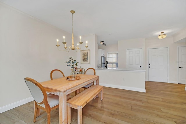 dining space with sink, light hardwood / wood-style floors, and an inviting chandelier