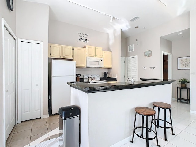 kitchen with tasteful backsplash, white appliances, a kitchen bar, a center island with sink, and light tile patterned floors