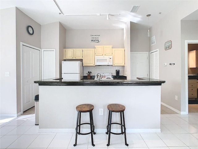 kitchen featuring sink, white appliances, a kitchen bar, decorative backsplash, and light tile patterned flooring