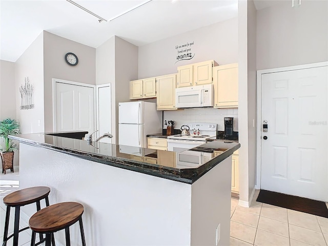 kitchen with white appliances, backsplash, light tile patterned floors, cream cabinetry, and a kitchen bar