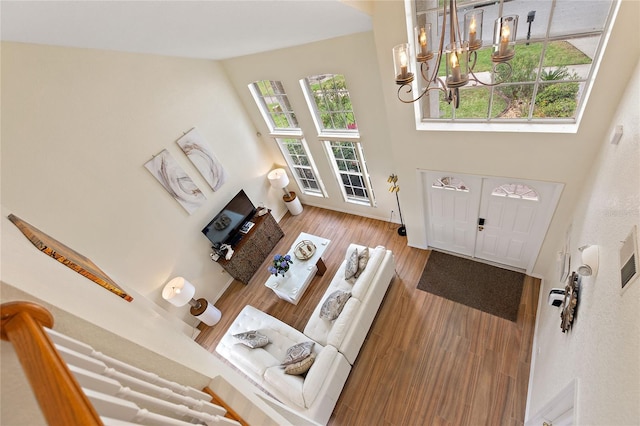 living room with a wealth of natural light, light hardwood / wood-style flooring, a towering ceiling, and an inviting chandelier