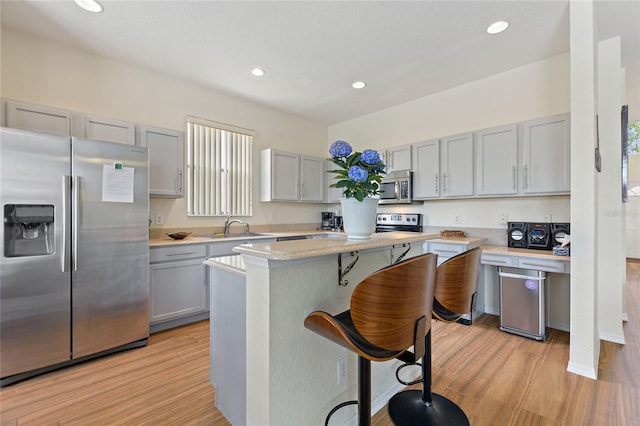 kitchen featuring sink, light hardwood / wood-style flooring, a breakfast bar, a kitchen island, and appliances with stainless steel finishes