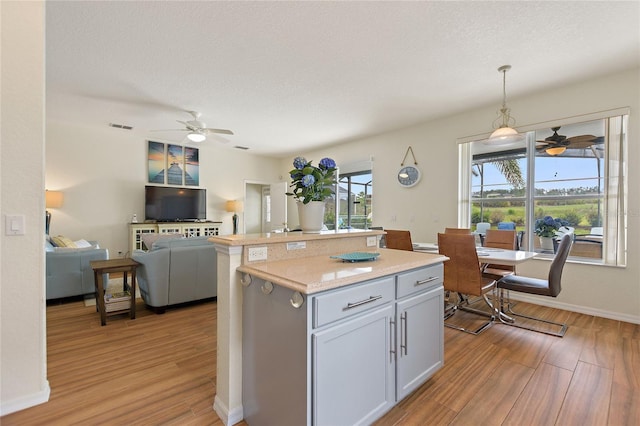 kitchen with a healthy amount of sunlight, a kitchen island, hanging light fixtures, and light hardwood / wood-style floors