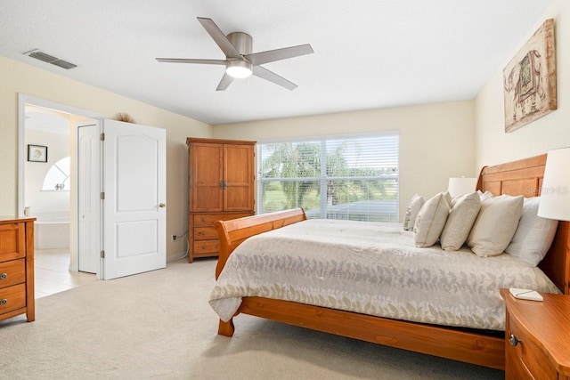 bedroom featuring ceiling fan, light colored carpet, and connected bathroom