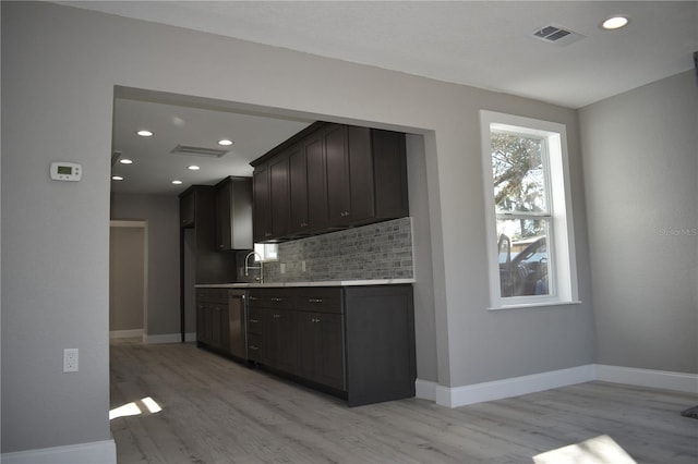 kitchen featuring tasteful backsplash, stainless steel dishwasher, dark brown cabinetry, sink, and light hardwood / wood-style floors