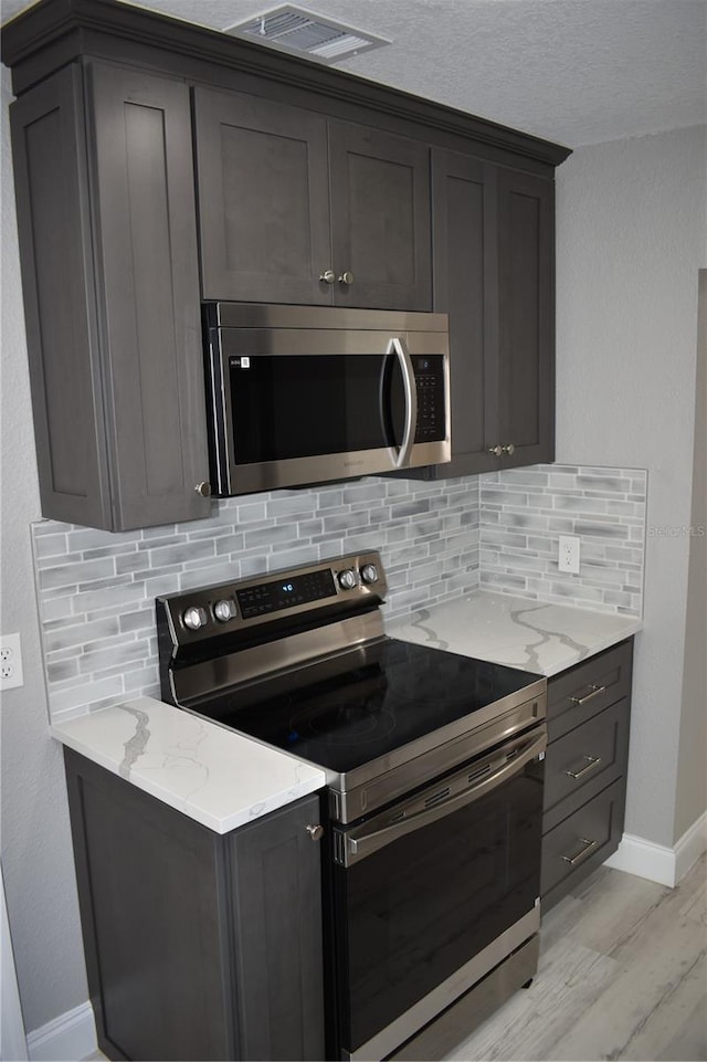 kitchen featuring backsplash, light stone counters, light hardwood / wood-style floors, and appliances with stainless steel finishes