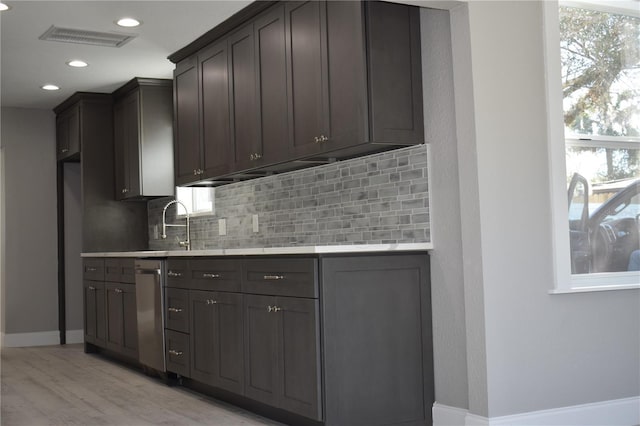 kitchen with dishwasher, decorative backsplash, dark brown cabinetry, and light hardwood / wood-style flooring