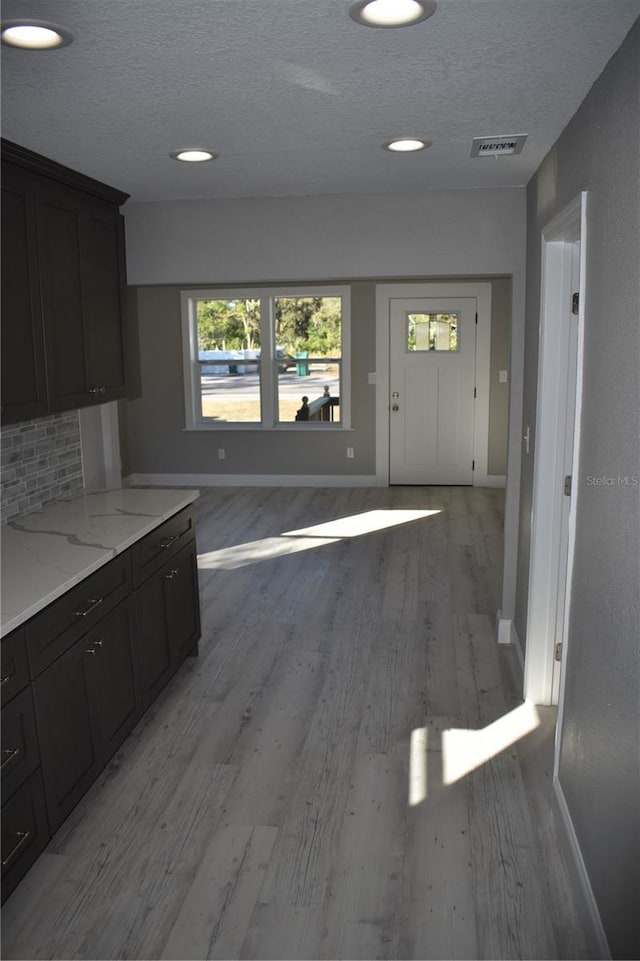 kitchen with decorative backsplash, a textured ceiling, light hardwood / wood-style flooring, and light stone countertops