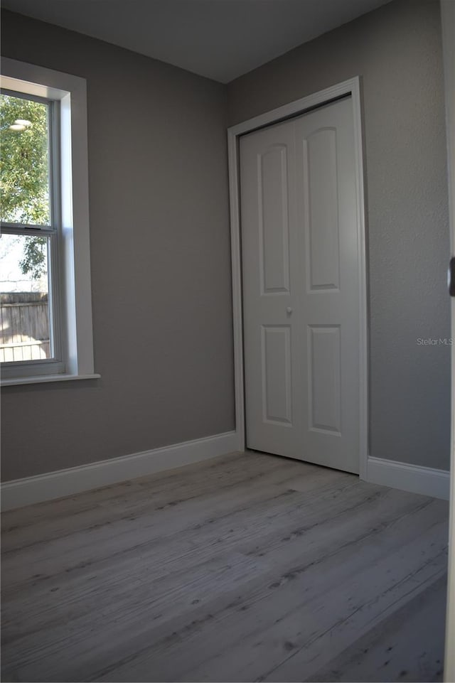 unfurnished bedroom with multiple windows, a closet, and light hardwood / wood-style floors