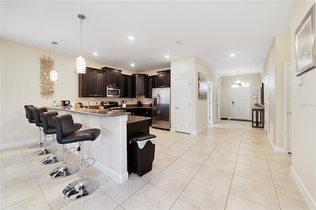 kitchen featuring hanging light fixtures, stainless steel appliances, kitchen peninsula, a breakfast bar area, and light tile patterned floors