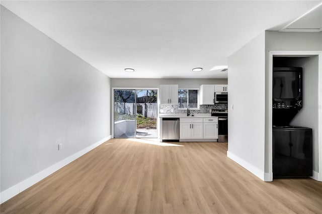 kitchen featuring stacked washer / dryer, stainless steel appliances, decorative backsplash, sink, and white cabinetry