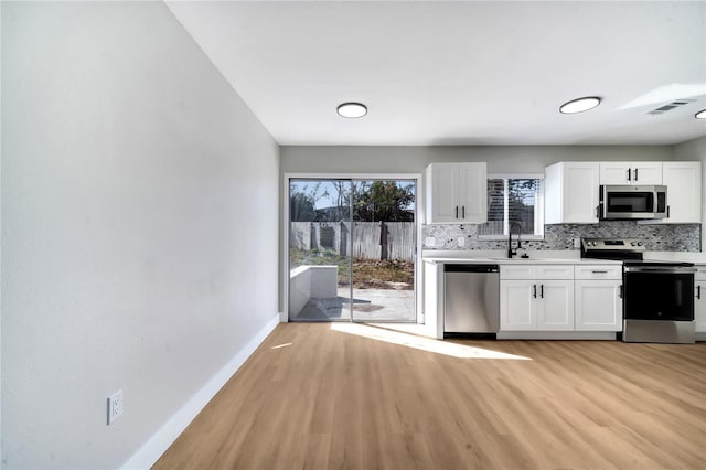 kitchen with light hardwood / wood-style floors, backsplash, white cabinets, appliances with stainless steel finishes, and sink