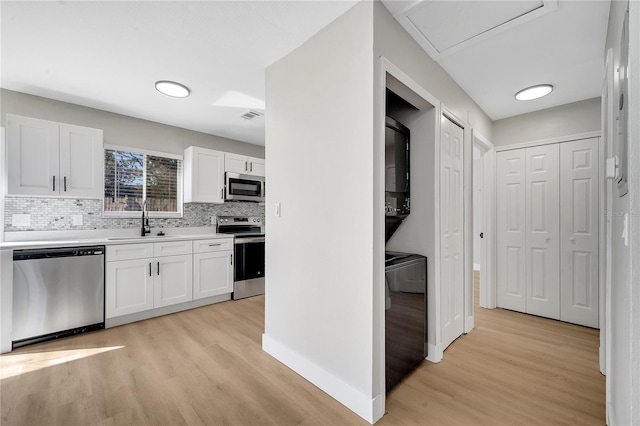 kitchen featuring stainless steel appliances, stacked washer / drying machine, white cabinets, light hardwood / wood-style flooring, and sink