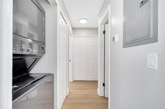 laundry area featuring stacked washing maching and dryer, electric panel, and light hardwood / wood-style flooring