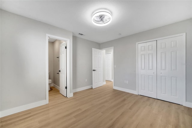 unfurnished bedroom with light hardwood / wood-style flooring, a closet, and ensuite bath