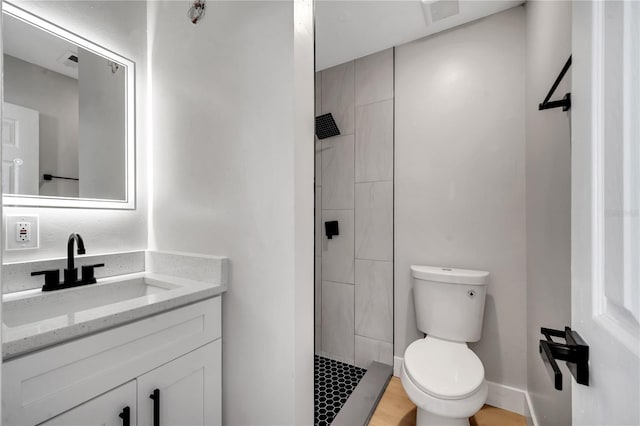 bathroom with toilet, a tile shower, and vanity