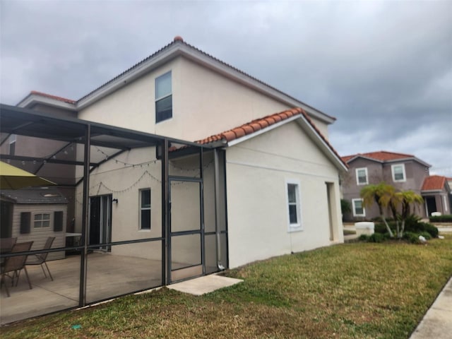 back of house featuring a lawn, glass enclosure, and a patio