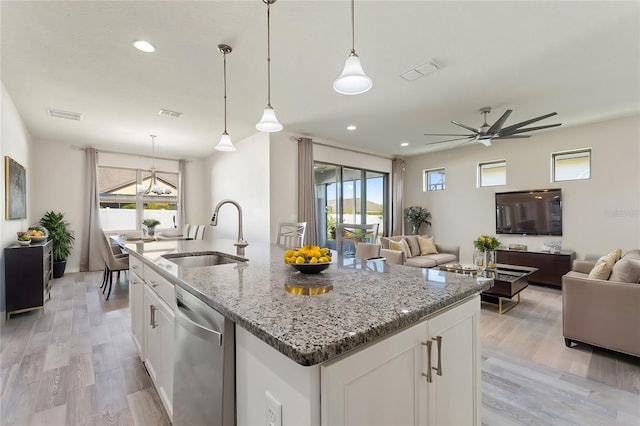 kitchen with white cabinets, decorative light fixtures, sink, stainless steel dishwasher, and a center island with sink