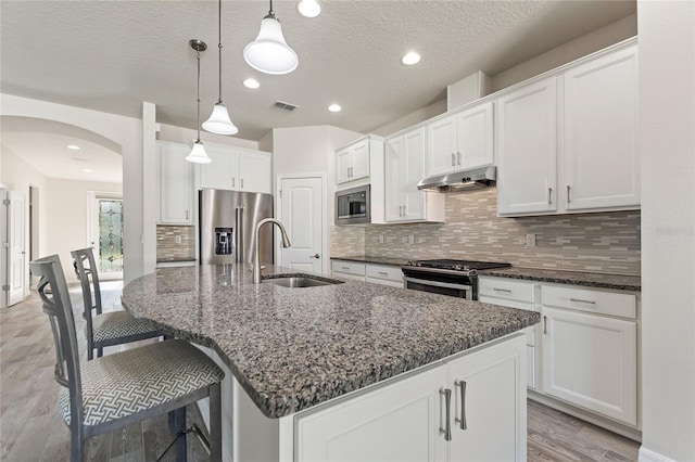 kitchen featuring white cabinetry, pendant lighting, appliances with stainless steel finishes, and a kitchen island with sink