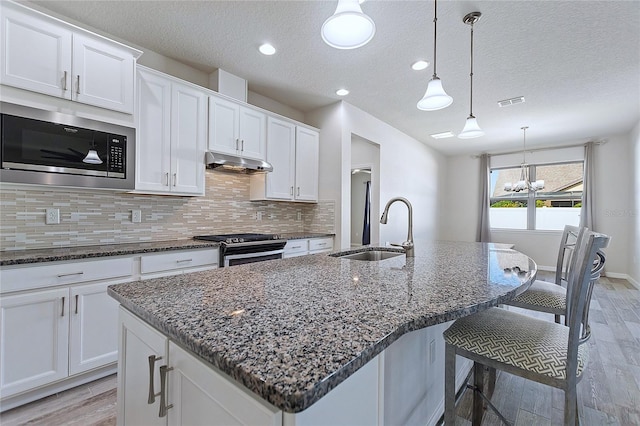 kitchen featuring dark stone countertops, sink, built in microwave, an island with sink, and stainless steel range oven