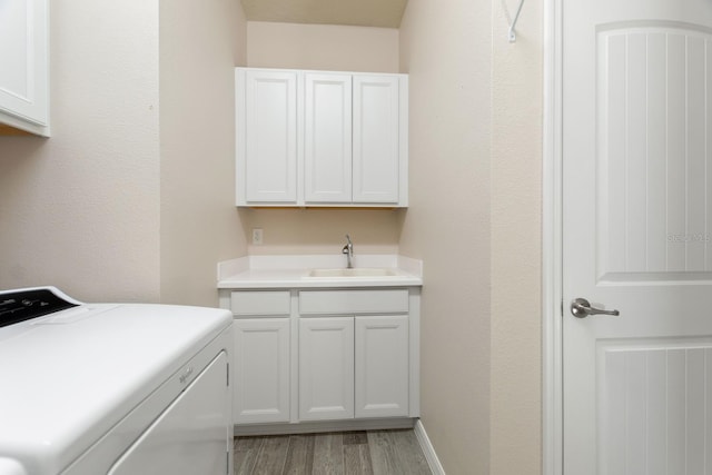 clothes washing area featuring washer / clothes dryer, sink, light hardwood / wood-style flooring, and cabinets