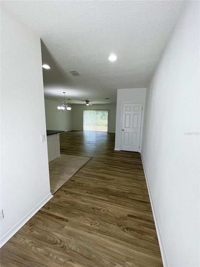 corridor with hardwood / wood-style floors, a textured ceiling, and an inviting chandelier