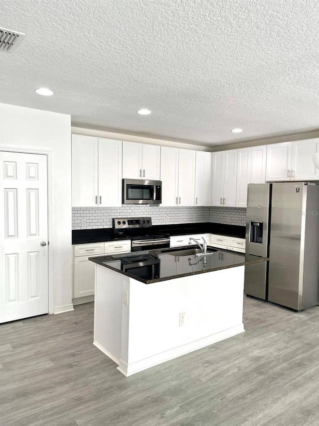 kitchen with a center island with sink, white cabinetry, appliances with stainless steel finishes, and light hardwood / wood-style flooring