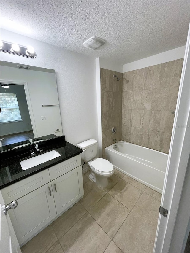 full bathroom featuring vanity, tile patterned floors, tiled shower / bath combo, toilet, and a textured ceiling