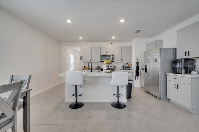 kitchen with a kitchen bar, appliances with stainless steel finishes, sink, light tile patterned floors, and a center island with sink