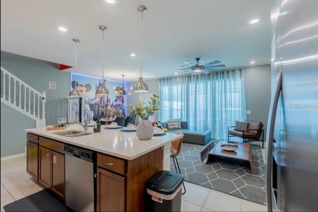 kitchen with stainless steel appliances, sink, hanging light fixtures, a kitchen island with sink, and light tile patterned floors