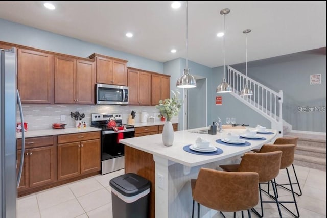 kitchen with a kitchen bar, a center island with sink, stainless steel appliances, decorative backsplash, and hanging light fixtures