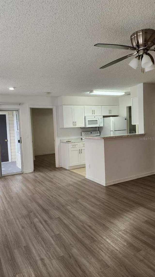 kitchen with kitchen peninsula, white appliances, white cabinetry, and dark wood-type flooring