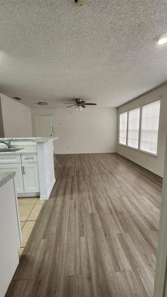 unfurnished living room featuring ceiling fan, sink, light hardwood / wood-style floors, and a textured ceiling