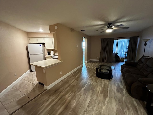 kitchen with kitchen peninsula, ceiling fan, white fridge, light hardwood / wood-style floors, and white cabinetry