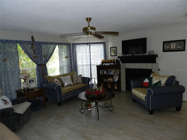 living room with a tile fireplace, a textured ceiling, and ceiling fan