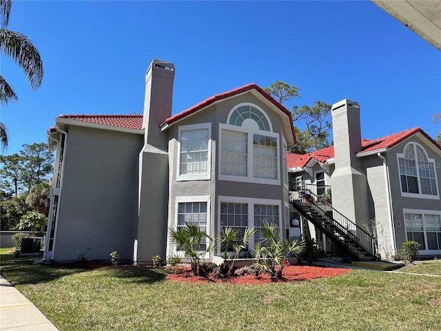 back of property featuring a chimney, stairs, stucco siding, a tiled roof, and a lawn