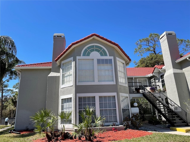 back of property with stucco siding, stairs, and a tile roof