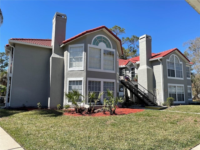 back of house with stucco siding, a lawn, a tile roof, stairway, and a chimney