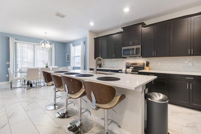 kitchen featuring a kitchen island with sink, sink, hanging light fixtures, a notable chandelier, and stainless steel appliances