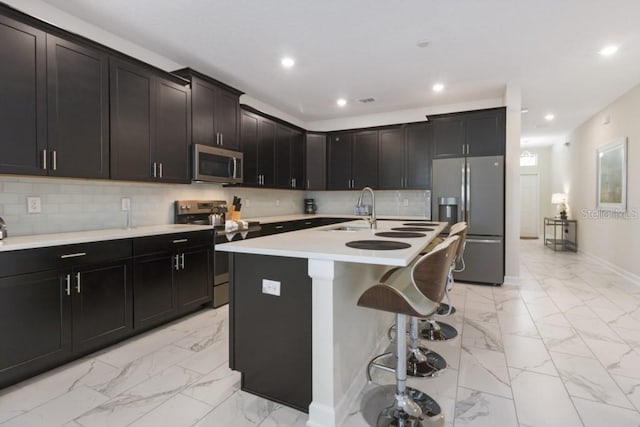 kitchen with backsplash, sink, an island with sink, appliances with stainless steel finishes, and a kitchen bar